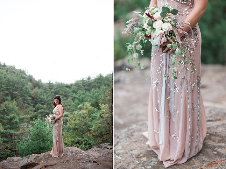 Bride on cliff in beaded gown, blue skirt, and shawl with bouquet