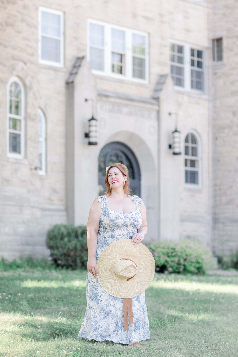 fine art film portrait of plus size redhead photographer in with a blue and white dress in front of a castle with a large hat.